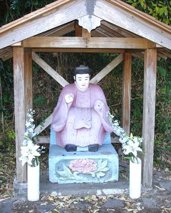 覆堂の下、両脇の花瓶に花がささげられている田の神像を正面から写した写真