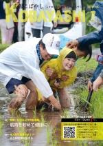 合羽を着て水田に膝下まで浸かりながら田植え体験を楽しむ人達の写真が掲載された広報こばやし7月号の表紙