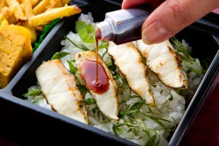 炙りチラシの上の魚の身に、備え付けのタレをかけている写真