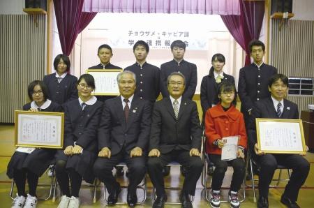 制服姿の学生たちとスーツ姿の男性3名が並んで記念撮影をしている写真