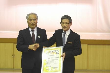 スーツ姿の男性2名が感謝状を手に、握手を交わしている写真