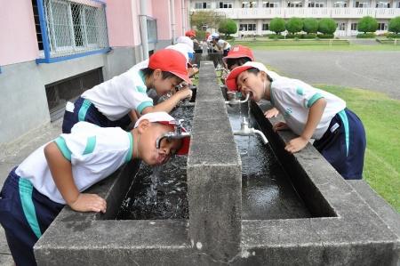 赤白帽子を被った児童たちが水道から水を飲んでいる写真