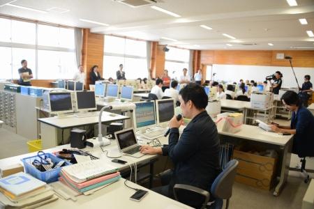 パソコンを操作しながらマイクを手に持って生徒たちに説明している男性の写真
