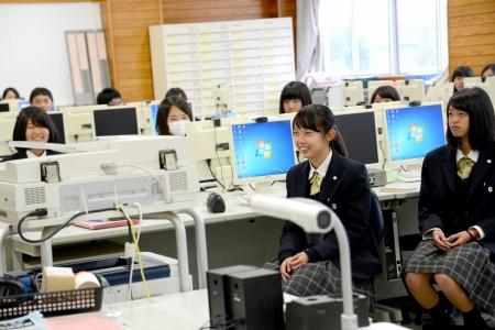 パソコンが並んだ教室で、生徒たちが着席している写真