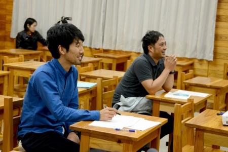青いシャツを着た男性と、グレーのシャツを着た男性が笑顔で着席している写真