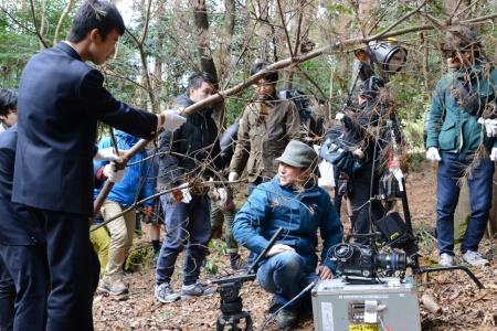 カメラの横で細い木を押し下げ、撮影の補助をしている男子生徒たちの写真