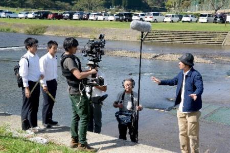 カメラやマイクなどの機材を手に取材をする生徒と大人たちの写真