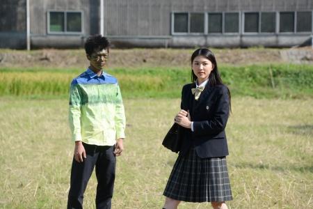 倉庫のような場所と草原で立つ男子と女子生徒の写真