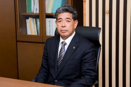 A photo of a seated man in a suit looking at the camera.