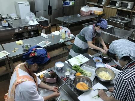 三角巾とエプロンをつけた参加者たちが調理をしている料理講座の写真