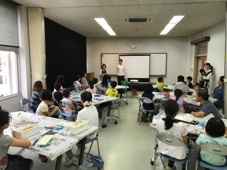 スクリーンのある教室内で参加者たちが講師の話を聞いている写真