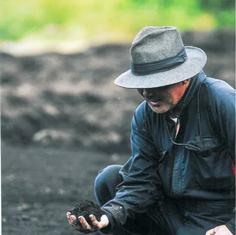 深く帽子をかぶった男性が土を手にしている写真