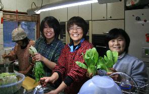 厨房で笑顔の女性たちが食材の野菜の下ごしらえをしている写真