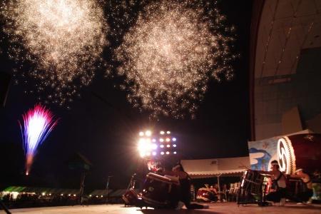 夜空に打ちあがる花火とステージを横から撮影した写真
