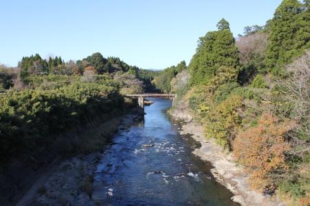 紅葉した木々と清流、橋を遠くに見下ろす自然風景の写真