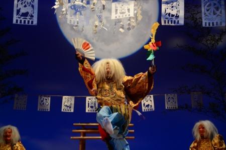 月の浮かぶ背景を背に神楽を踊る演者の写真