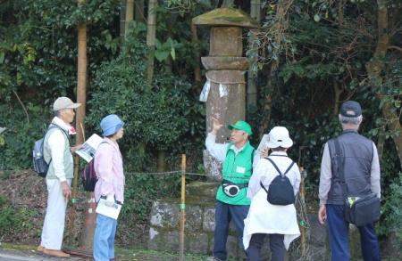 緑色の服を来たガイドの男性が石碑の前で説明をしている写真