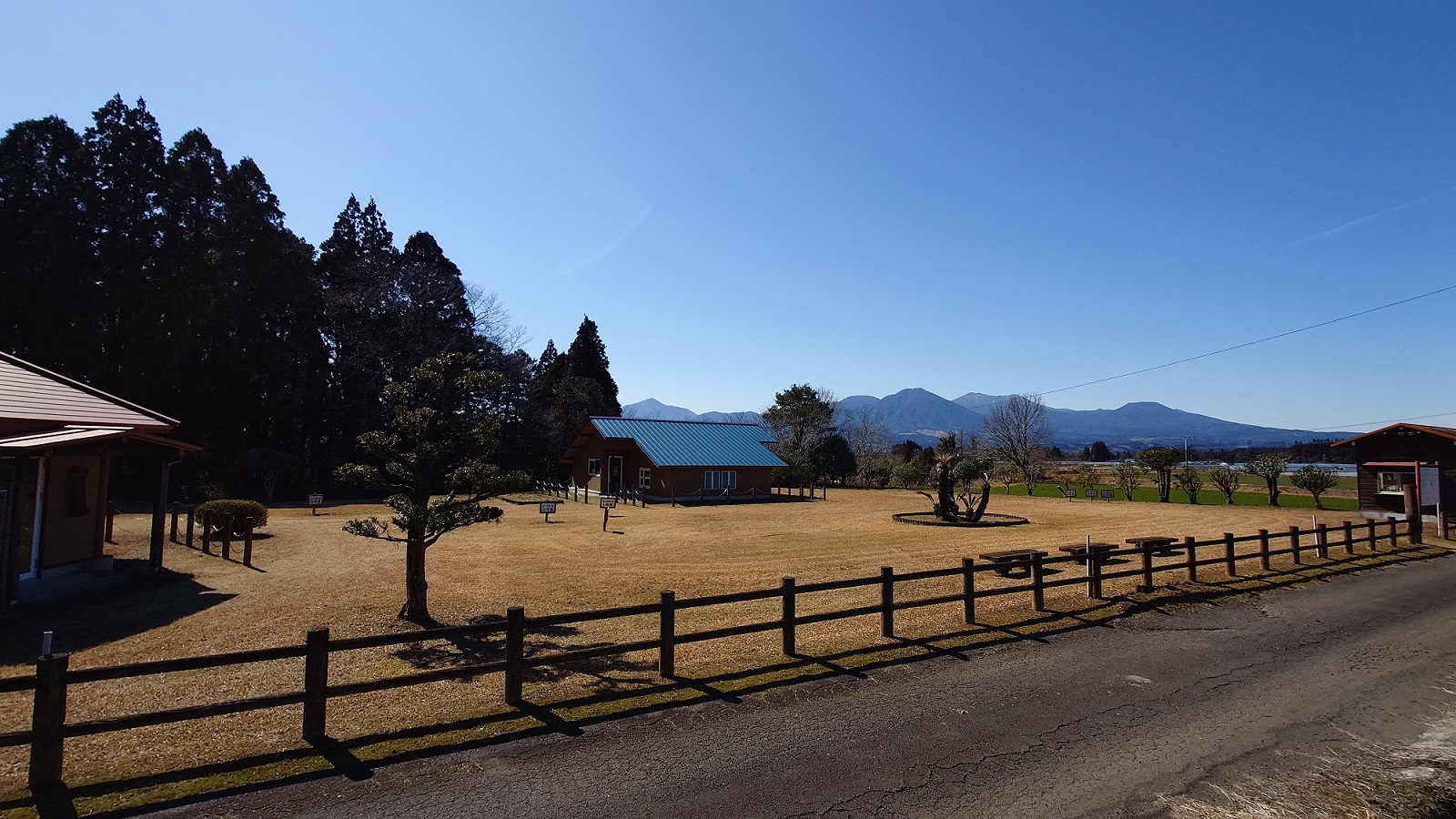 霧島連山をバックに木製の柵と小屋、芝生が広がっている写真