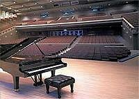 小林市文化会館大ホールの舞台上に置かれたグランドピアノ越しに赤色の客席を撮影した写真