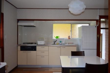 光が差し込む窓側にフロンティア荘キッチンがあり、右手に白い冷蔵庫、手前にモノトーンの机といすが写っている写真