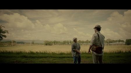 広い田んぼのそばでおばあちゃんと男性が立っている写真