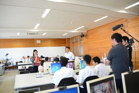 パソコンの前に座っている生徒たちと、その様子を撮影している多くの報道陣の写真