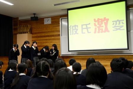 「彼氏激変」と文字が表示されたスクリーンと、その横に立ってプレゼンテーションをしている女子生徒たちと、座って聞いている生徒たちの写真