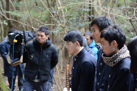 林の中で、撮影の様子を熱心に見学している男子生徒たちの写真