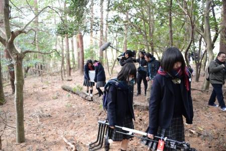 林の中で、二人がかりで撮影機材を運搬している女子生徒たちの写真