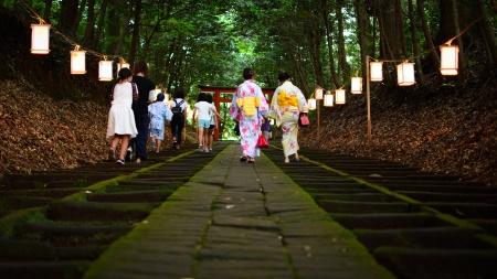 行灯の灯る神社の参道を浴衣姿の女性たちが歩いている写真