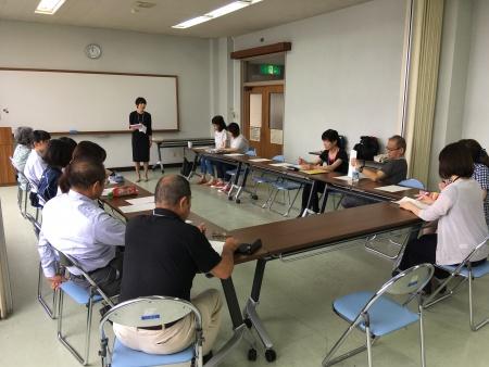 A picture of the participants sitting around a row of U-shaped desks and taking a class