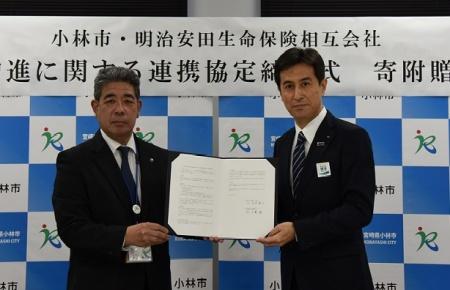 スーツ姿の市長と明治安田生命保険相互会社代表の男性が締結式を行っている写真